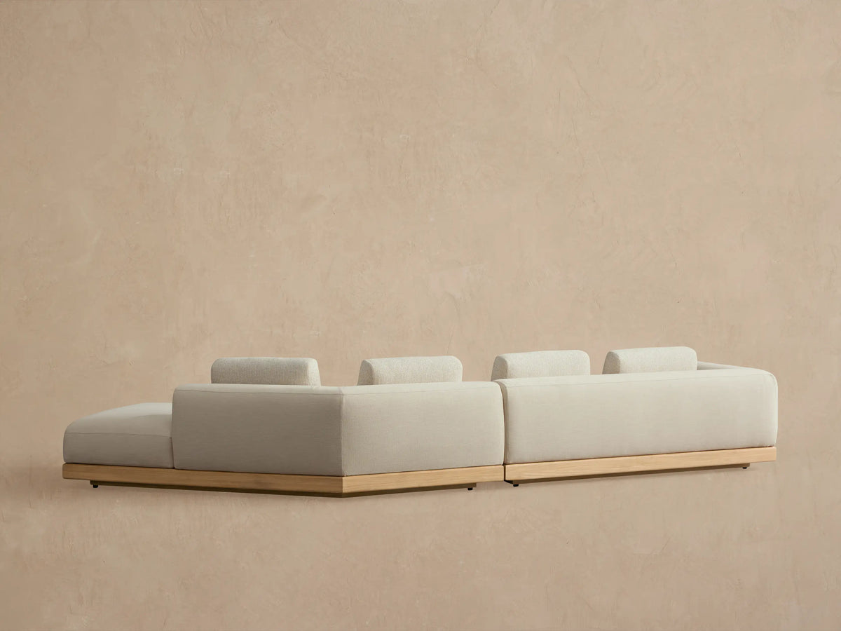 Carmel Outdoor Two-Piece Bumper Sectional with light beige cushions, teak base, and two lumbar pillows.