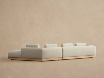 Carmel Outdoor Two-Piece Bumper Sectional with light beige cushions, teak base, and two lumbar pillows.