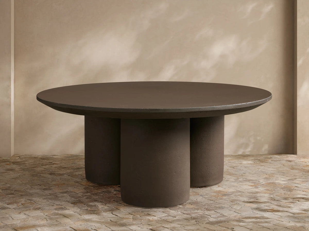 Cascade Outdoor Coffee Table, round, dark brown with a beveled edge, supported by three thick cylindrical legs, on a tiled patio.