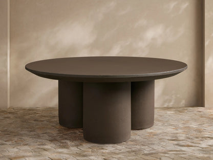 Cascade Outdoor Coffee Table, round, dark brown with a beveled edge, supported by three thick cylindrical legs, on a tiled patio.