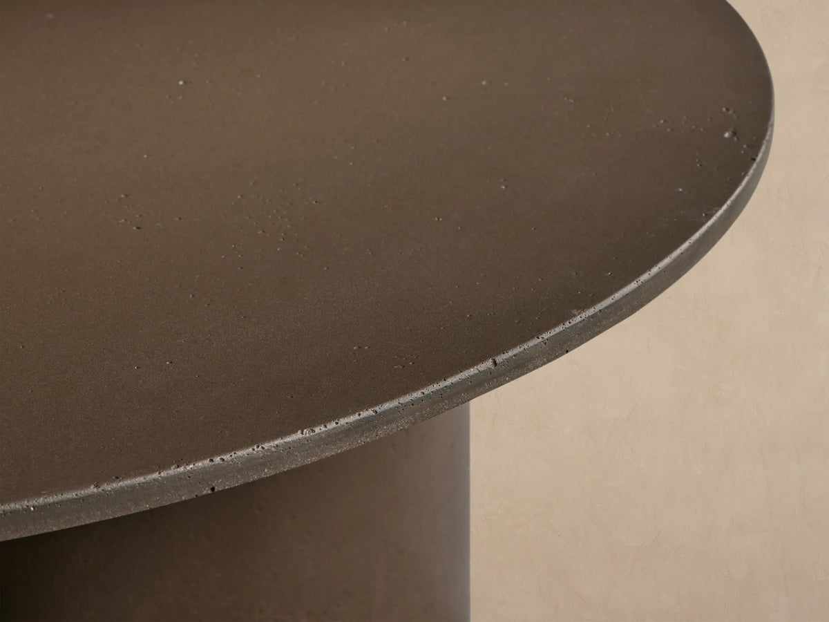 Cascade Outdoor Coffee Table, round dark brown, with reverse-beveled top & three column-style legs on tiled floor.