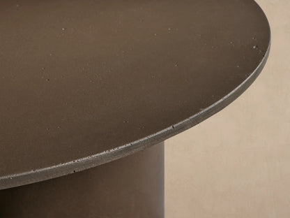 Cascade Outdoor Coffee Table, round dark brown, with reverse-beveled top & three column-style legs on tiled floor.