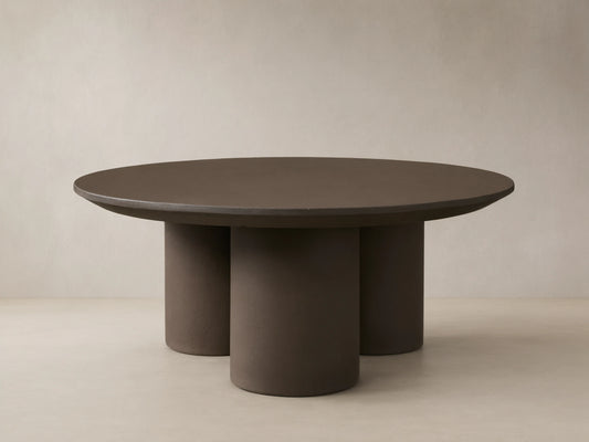 Cascade Outdoor Coffee Table, round, dark brown with a beveled edge, supported by three thick cylindrical legs, on a tiled patio.