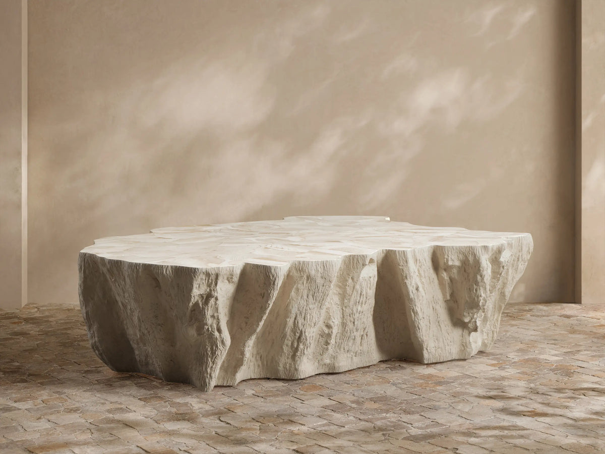 Clayhill Outdoor Coffee Table with a light, organic, tree trunk-like design, centered in an outdoor patio seating area with lush plants.