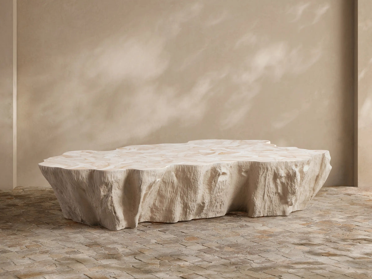Light, organic-shaped Clayhill Outdoor Coffee Table with a textured top, central on a patio with natural woven seating and white hydrangeas.