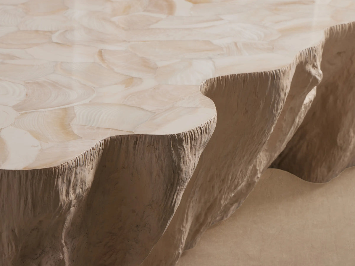 Clayhill Outdoor Coffee Table, organically shaped, light beige, with a rough, natural-looking base and mosaic top, on a stone paved floor.