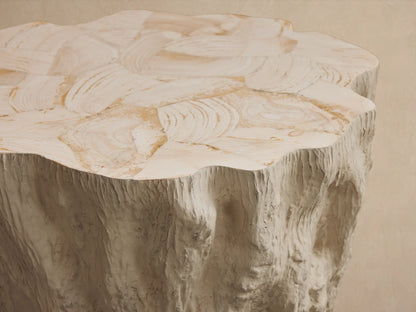Light beige textured Clayhill Outdoor Tapered End Table, shaped like a tree stump, on stone pavers.