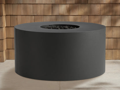 Round, dark gray Coden Outdoor Propane Fire Pit with bright orange and yellow flames burning in the center. Wooden wall in background.