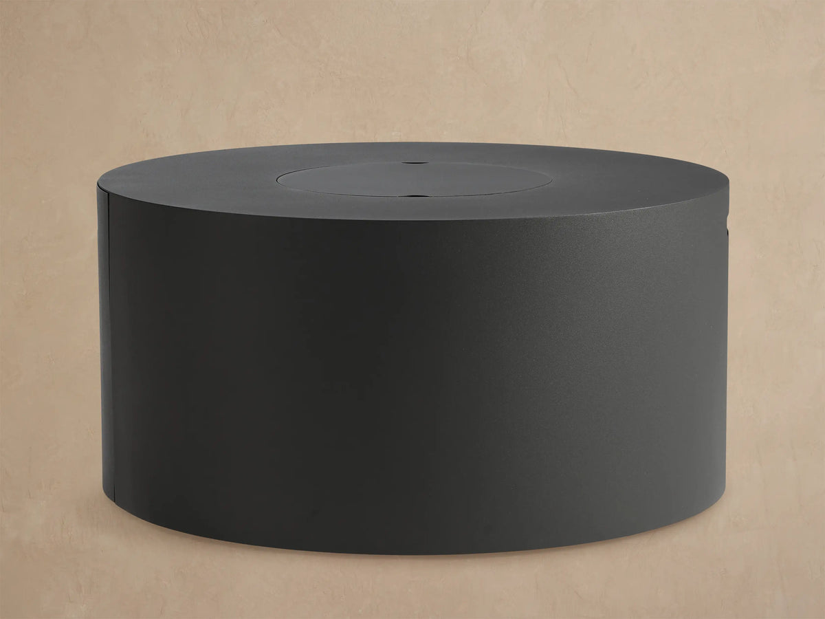 Coden Outdoor Round Propane Fire Pit, dark gray cylindrical design, with black lava rock inside, on a patio.