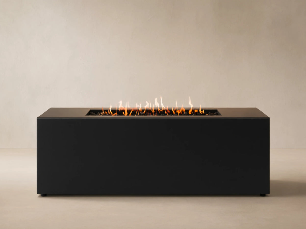 Coden Rectangular Propane Fire Pit in dark grey with orange flames rising from black lava rocks, against a wooden wall.