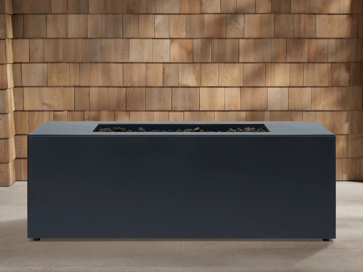 Coden Rectangular Natural Gas Fire Pit, dark gray, with vibrant flames burning in a central trough against a wooden wall.