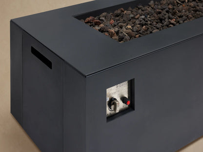 Coden Rectangular Natural Gas Fire Pit in dark gray, with black lava rocks, centered on a patio floor against a wooden shingle wall.
