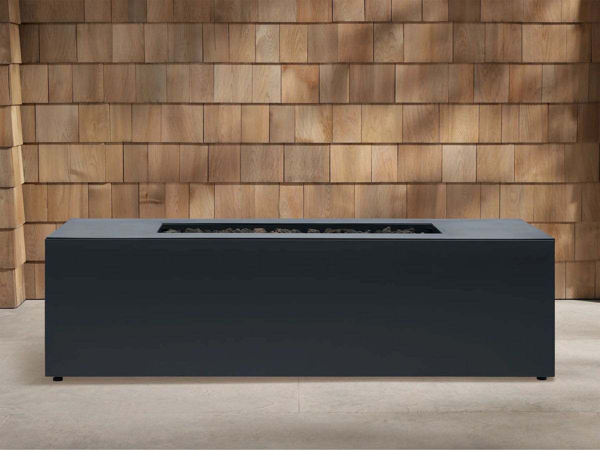 Dark gray Coden Rectangular Propane Fire Pit with burner opening, subtly lit from below, against a wooden shingle wall.