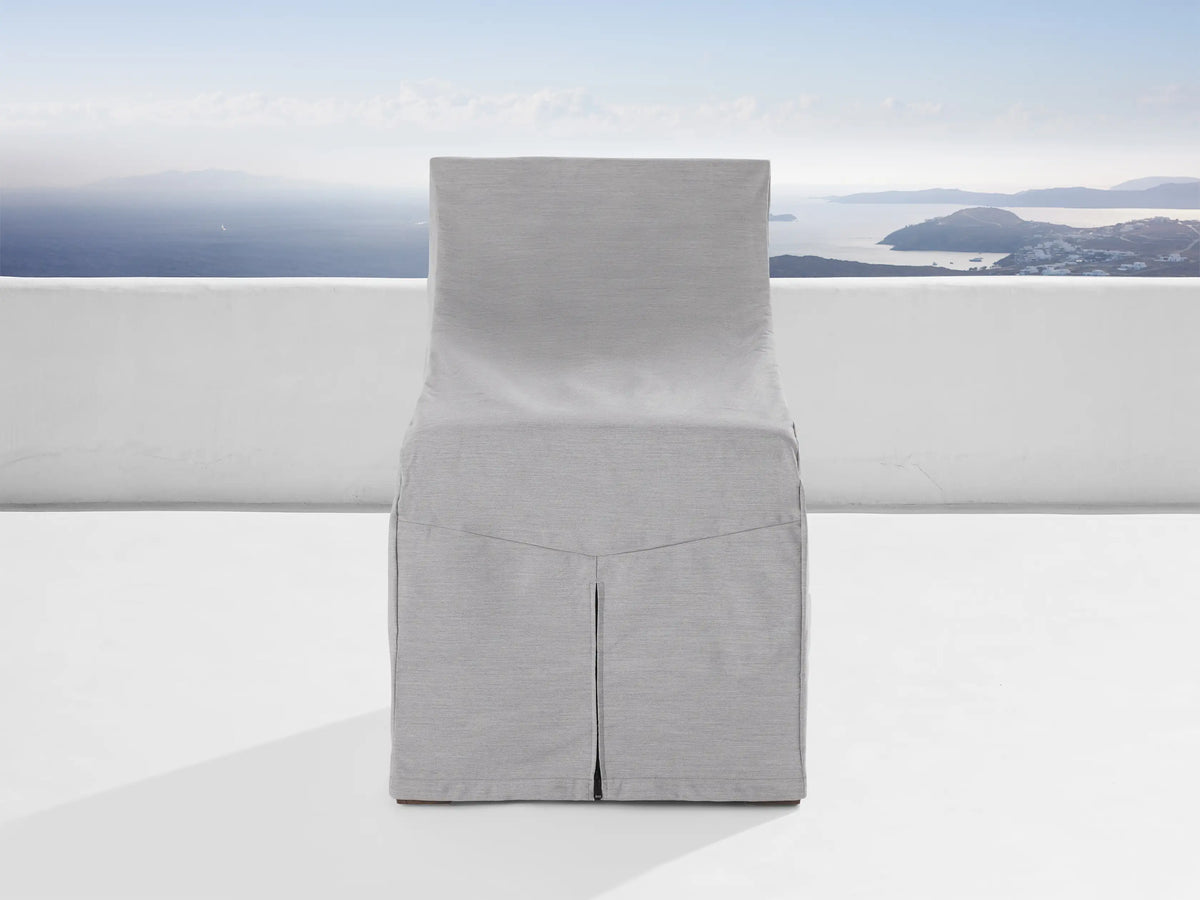 A light gray protective cover from the Del Ray Outdoor Collection snugly fits over a chair. The background shows a scenic ocean view.