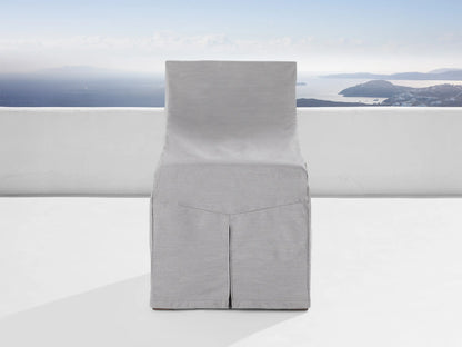 A light gray protective cover from the Del Ray Outdoor Collection snugly fits over a chair. The background shows a scenic ocean view.