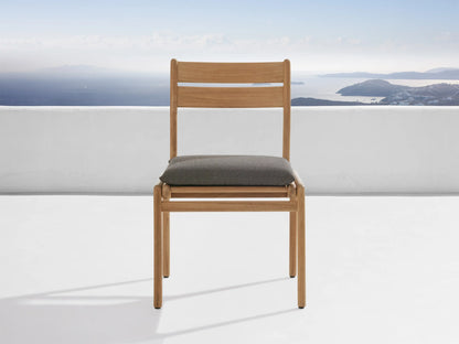 A light gray protective cover from the Del Ray Outdoor Collection snugly fits over a chair. The background shows a scenic ocean view.