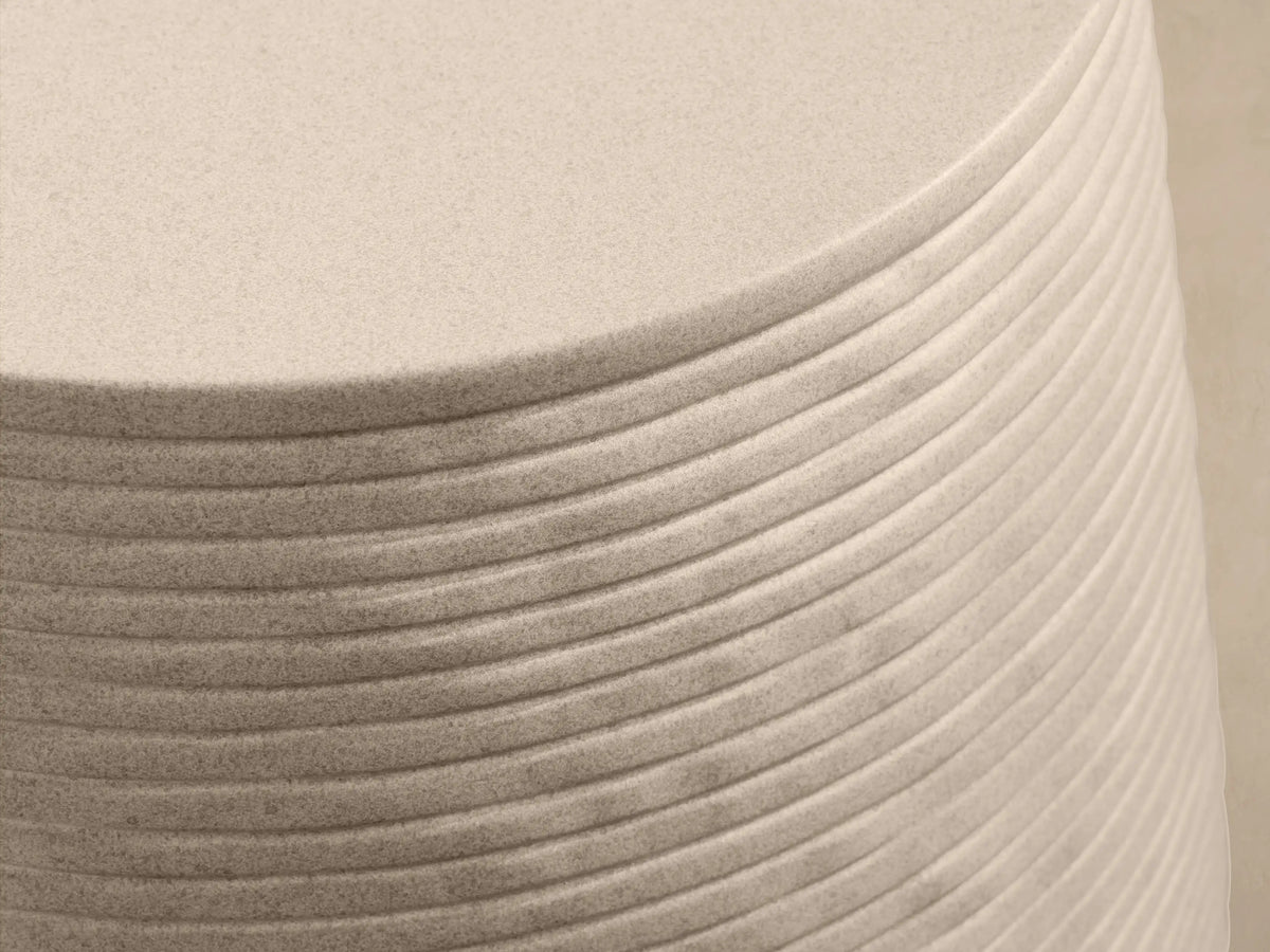 Eden Outdoor End Table. Light tan, round concrete table with distinct horizontal ribbed sides, on a stone patio.