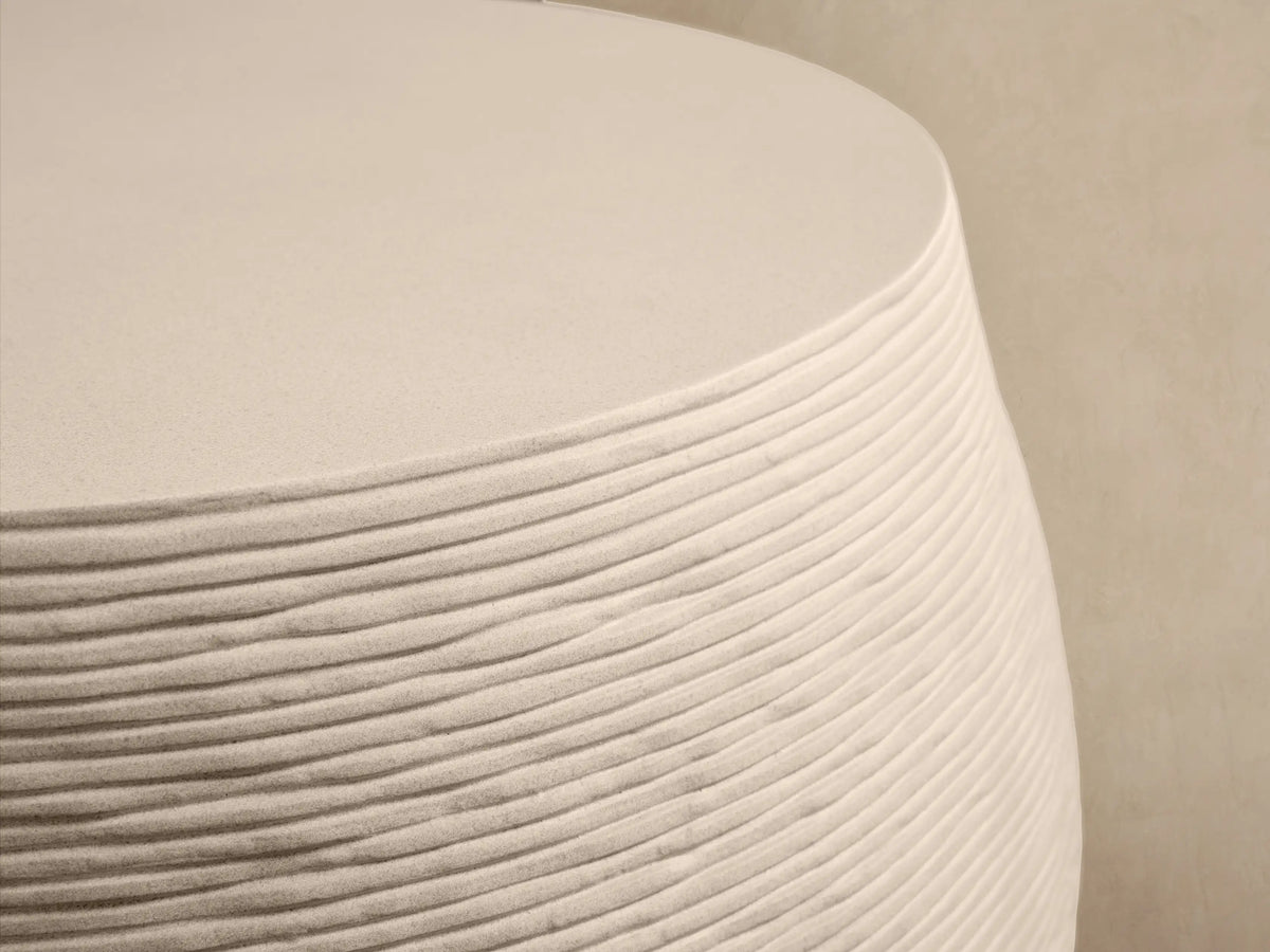 Eden Outdoor Round Coffee Table, light beige, drum-shaped with horizontal raked texture on sides, smooth top, on stone patio.
