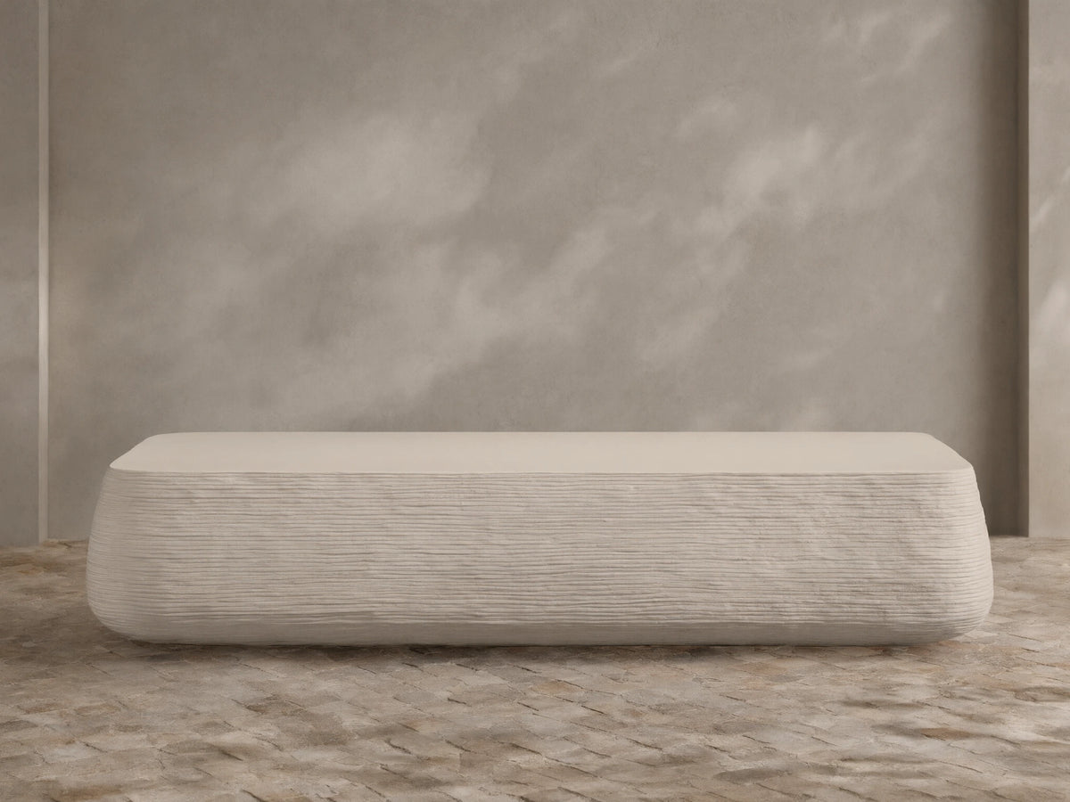 Eden Outdoor Coffee Table, off-white, rectangular with rounded edges, horizontal ribbed texture on sides, against tan wall and stone floor.