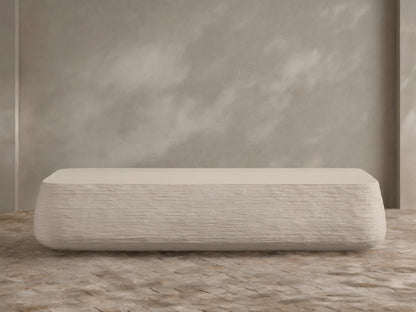 Eden Outdoor Coffee Table, off-white, rectangular with rounded edges, horizontal ribbed texture on sides, against tan wall and stone floor.