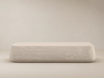 Eden Outdoor Coffee Table, off-white, rectangular with rounded edges, horizontal ribbed texture on sides, against tan wall and stone floor.