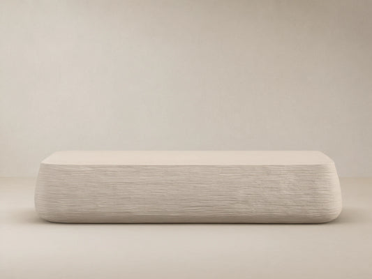 Eden Outdoor Coffee Table, off-white, rectangular with rounded edges, horizontal ribbed texture on sides, against tan wall and stone floor.