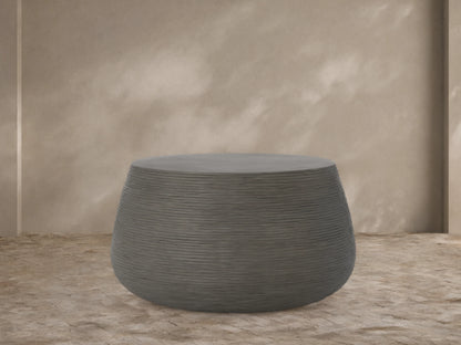 Dark grey Eden Outdoor Round Coffee Table with textured ribbed sides and smooth top, on a light brown tiled patio.