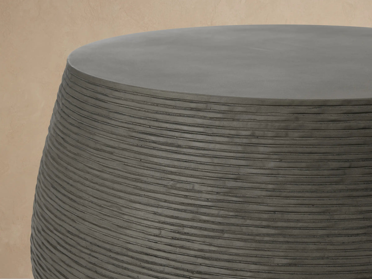 Dark grey Eden Outdoor Round Coffee Table with textured ribbed sides and smooth top, on a light brown tiled patio.