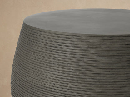 Dark grey Eden Outdoor Round Coffee Table with textured ribbed sides and smooth top, on a light brown tiled patio.