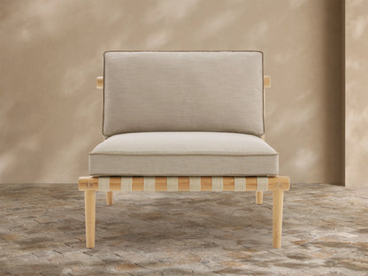 Elio Outdoor Lounge Chair with natural teak frame, light beige piped cushions, and woven seat support on a patio.