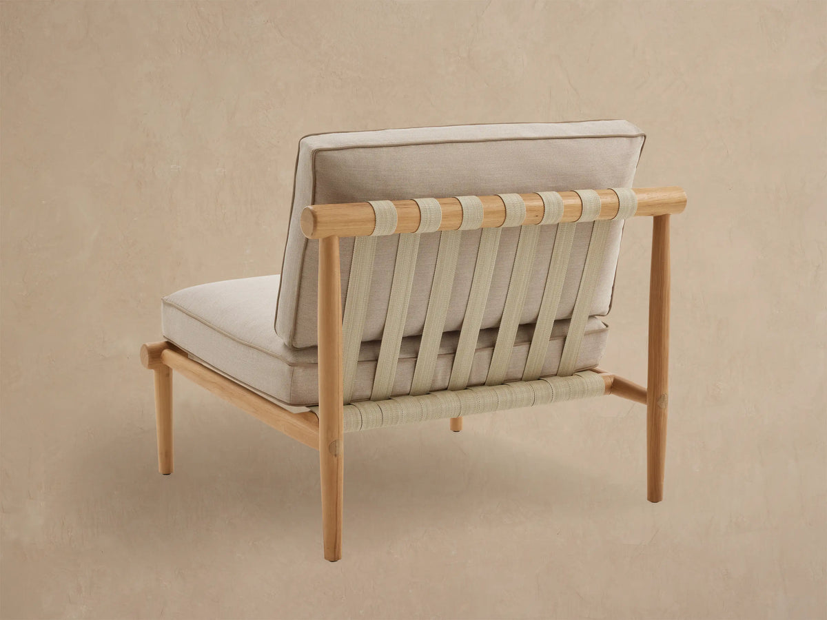 Elio Outdoor Lounge Chair, angled view of back. Light teak frame with beige woven straps and light beige cushion.