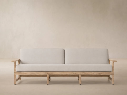 Front view of the Starboard Snow Emmons Outdoor Sofa with light white cushions and a natural teak wood frame.