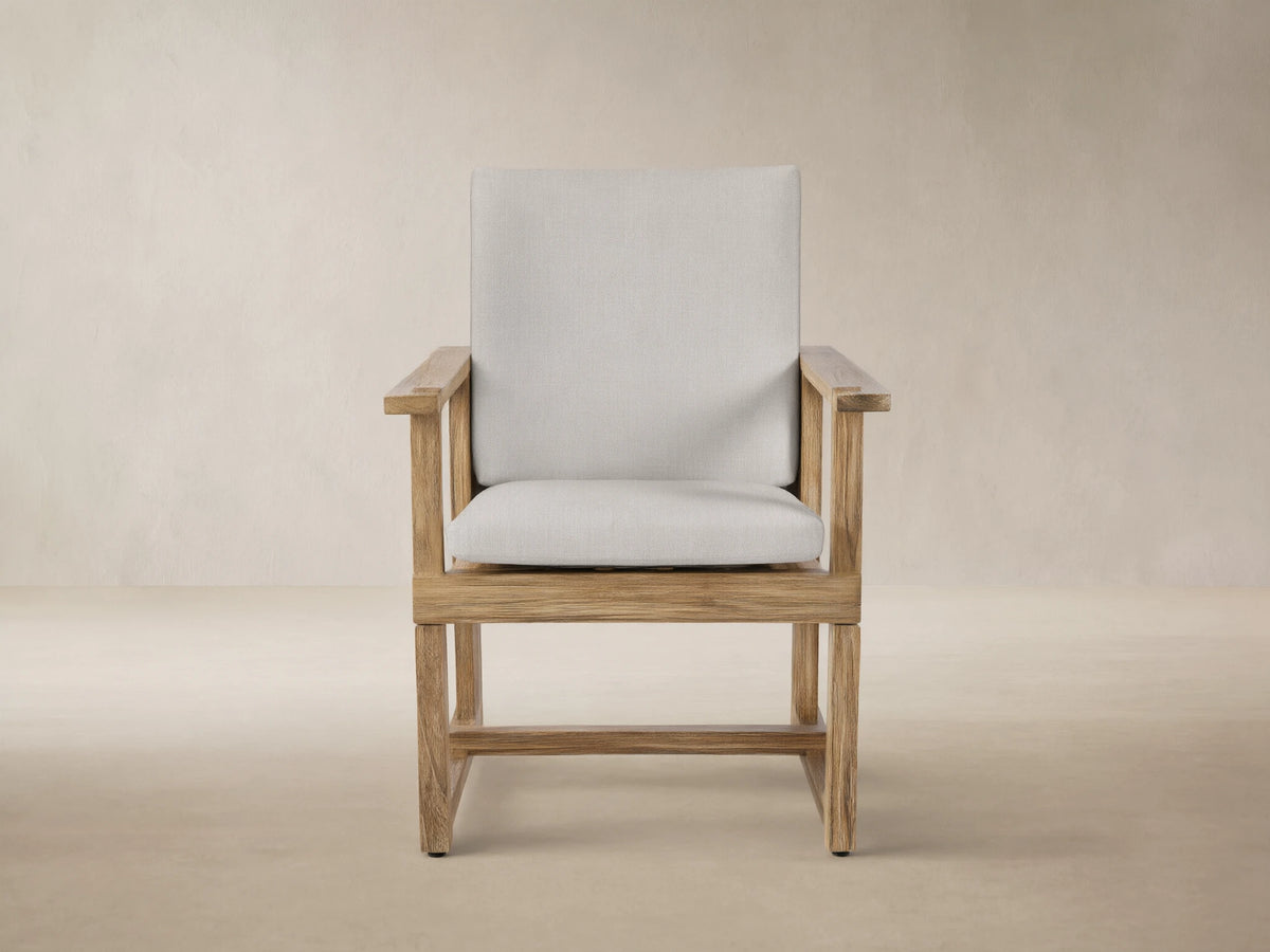 Front view of Starboard Snow Emmons Outdoor Dining Arm Chair with a natural teak wood frame and light grey cushions.