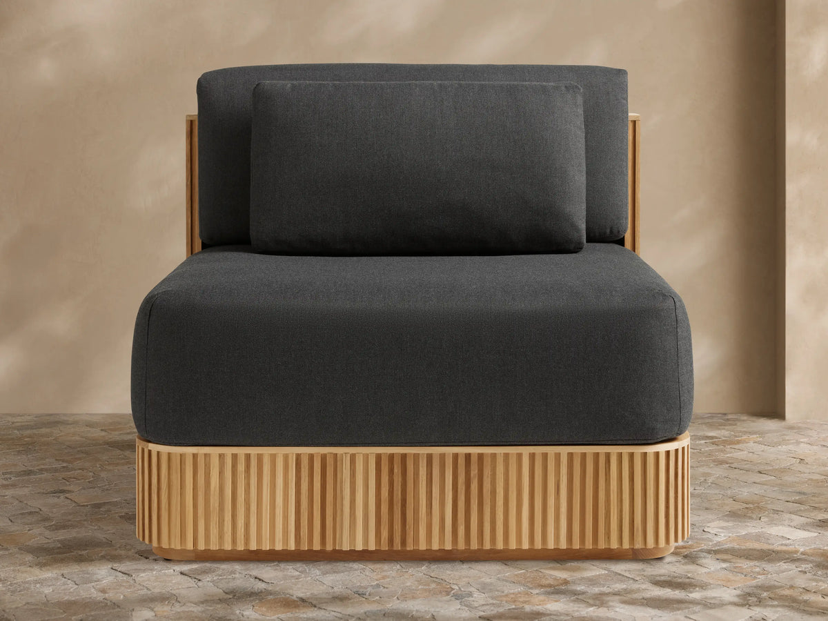 Beaumont Outdoor Teak Lounge Chair in Rosemount Graphite. Front-right view of dark grey cushions on a slatted light teak wood base.