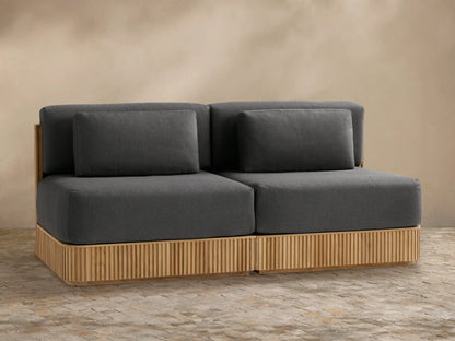 Beaumont Outdoor Teak Two-Piece Modular Sofa. Natural teak slatted base, dark grey cushions, front view against a beige wall.