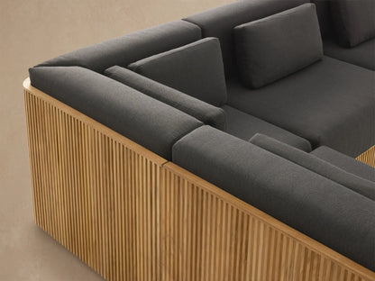 Beaumont Outdoor Teak Six-Piece Sectional with Chaise: L-shaped, natural slatted teak base, dark grey cushions, on a light patio.