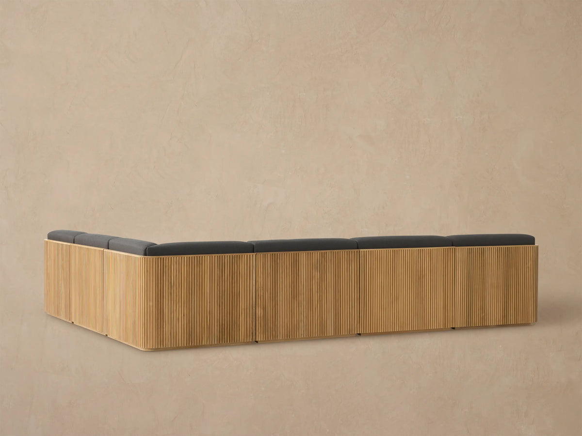 Close-up of Beaumont Outdoor Teak Sectional corner with natural slatted frame and dark grey cushions, viewed from above.