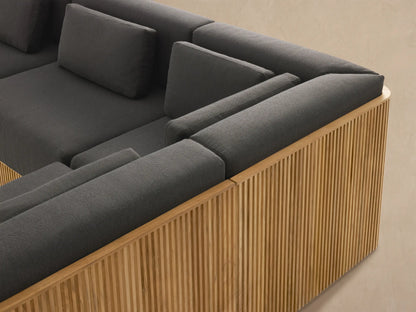 Beaumont Outdoor Teak Six-Piece Sectional with Chaise, L-shaped, dark gray cushions, slatted natural teak base on a stone patio.