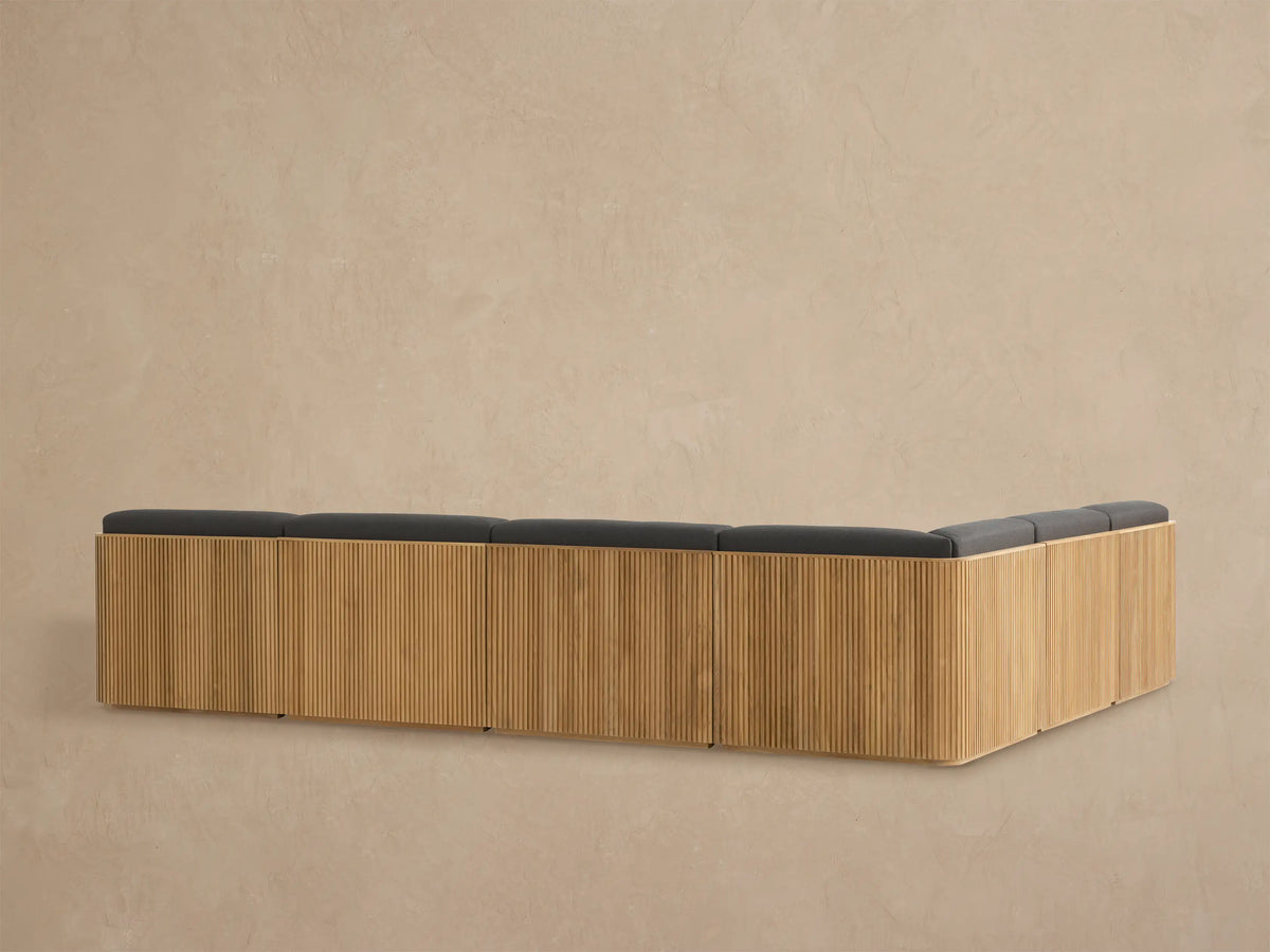 Close-up of Beaumont Outdoor Teak Sectional corner. Golden slatted teak frame and dark grey textured cushions.