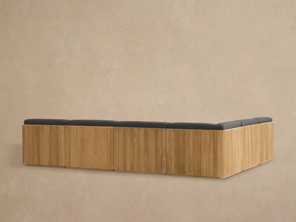 Close-up of Beaumont Outdoor Teak Sectional corner. Golden slatted teak frame and dark grey textured cushions.