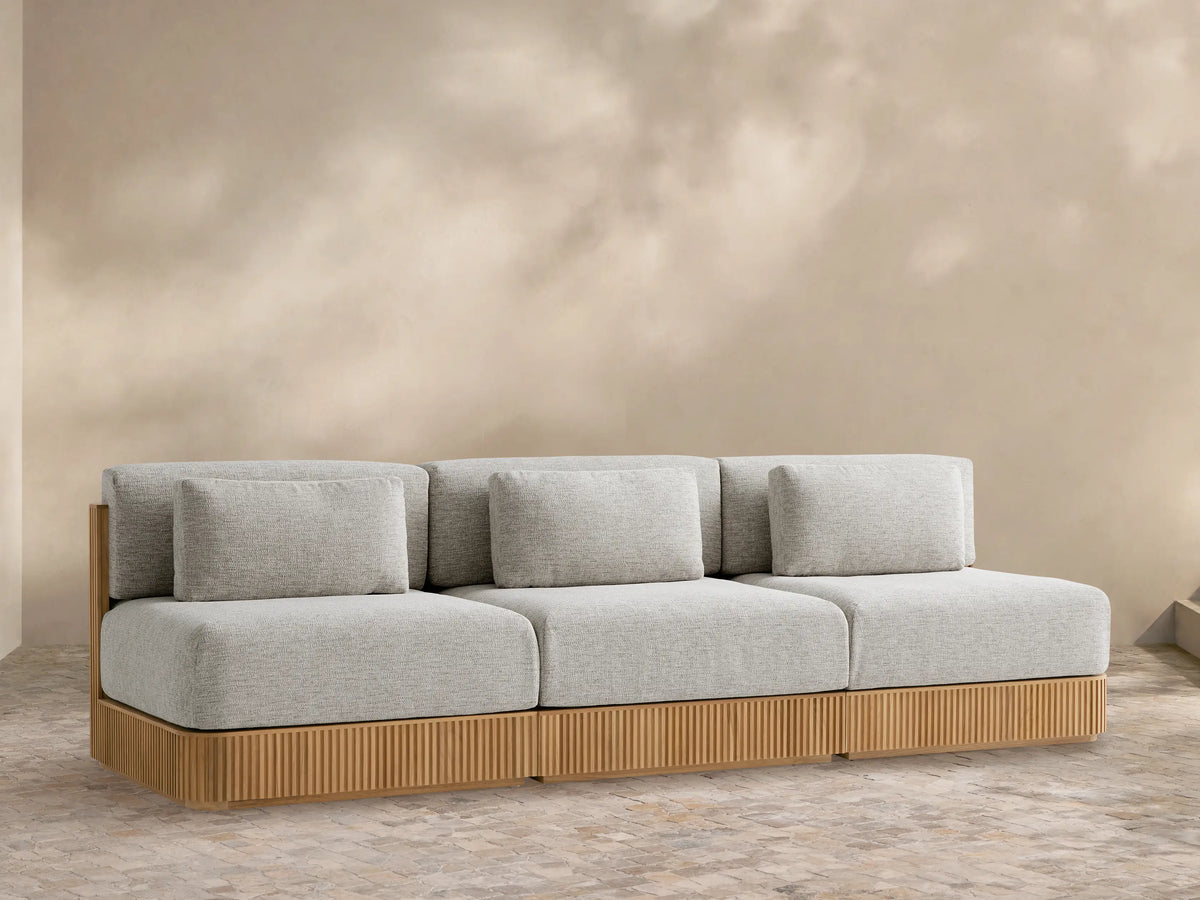 Beaumont Outdoor Teak Three-Piece Modular Sofa, with light grey cushions and slatted natural teak base, on a stone patio.