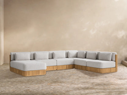 Beaumont Teak Six-Piece Sectional with Chaise, light grey cushions on slat-style natural teak base, L-shaped, against a beige wall.