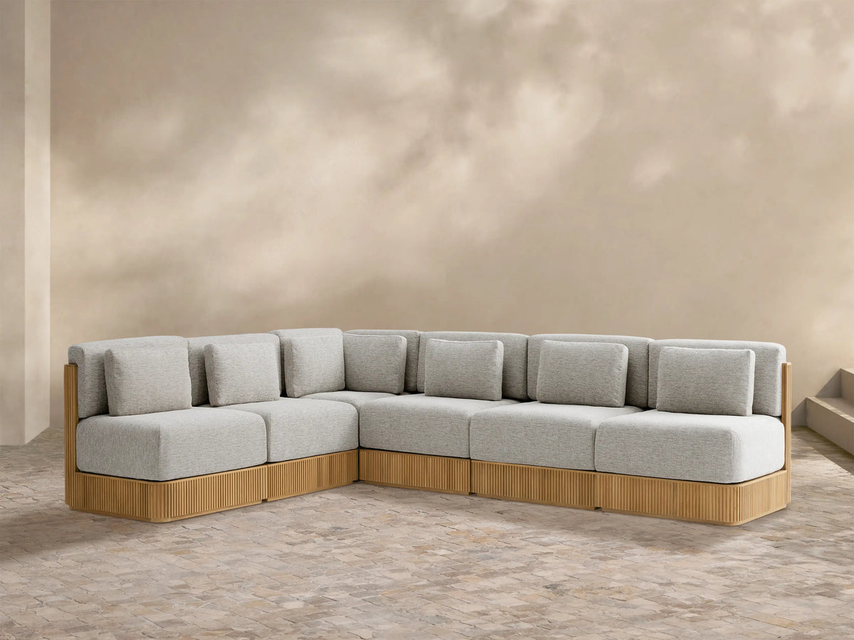 Beaumont Outdoor Teak Six-Piece Sectional, L-shaped, with light gray cushions and a fluted teak wood base on a patio.