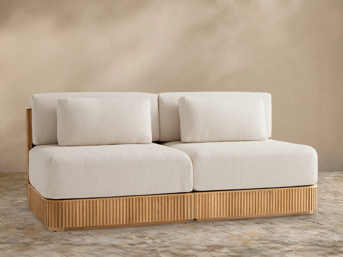 Beaumont Outdoor Teak Two-Piece Modular Sofa, front view. Light beige cushions on slatted natural teak wood base.