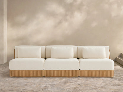 Beaumont Outdoor Teak Three-Piece Modular Sofa with light cream cushions & ribbed teak base on a tiled patio, beige wall behind.