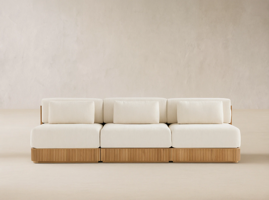 Beaumont Outdoor Teak Three-Piece Modular Sofa with light cream cushions & ribbed teak base on a tiled patio, beige wall behind.