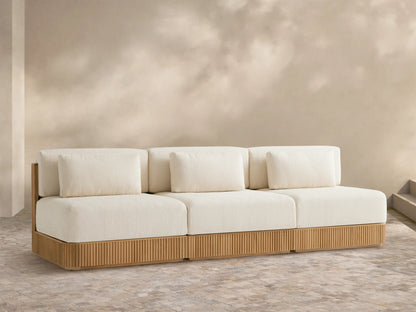 Beaumont Outdoor Teak Three-Piece Modular Sofa with light cream cushions & ribbed teak base on a tiled patio, beige wall behind.