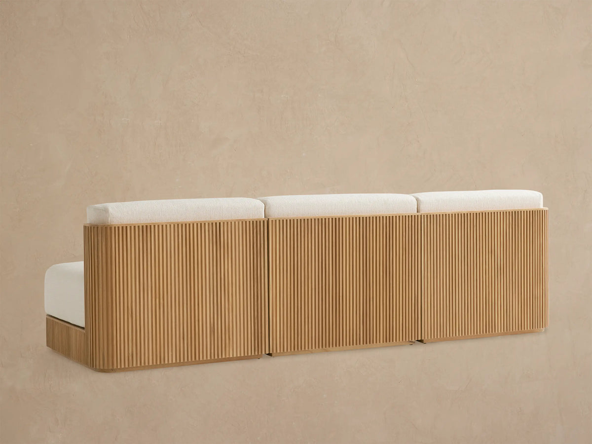Close-up of Beaumont Outdoor Teak Sofa section with cream textured cushions and slatted natural teak armrest, angled.