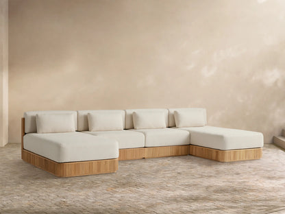 Beaumont Four-Piece Double Chaise Sectional, light cream cushions on a slatted natural teak base, against a beige wall on a patio.