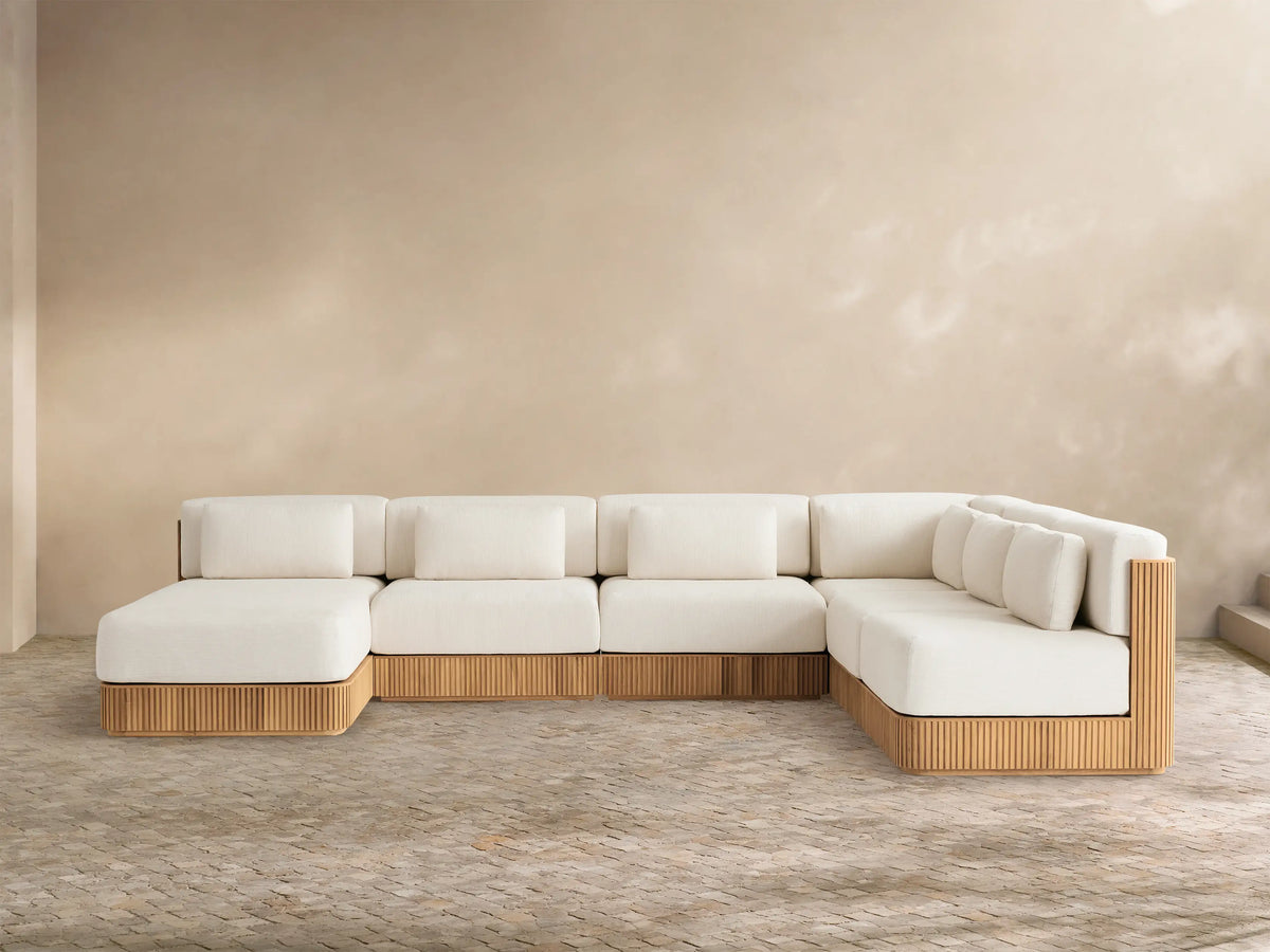 L-shaped Beaumont Teak Sectional with chaise, cream cushions, ribbed golden-brown teak base, on a paved patio.